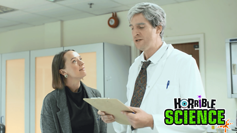 A woman looking up at a man in a white scientist coat reading from a clipboard