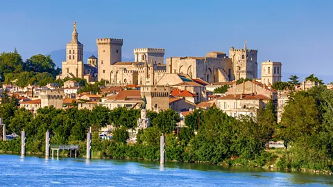 Getty Images A view of the Palais des Papes in Avignon, with trees and water beneath it (Credit: Getty Images)