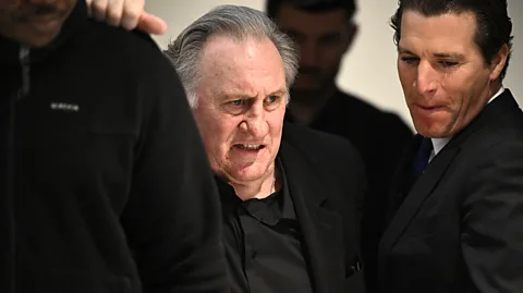 Getty Images Gérard Depardieu wearing a black suit with a policeman behind him (Credit: Getty Images)