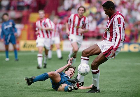 Brian Deane in a red and white Sheffield United kit tackling a player on the pitch