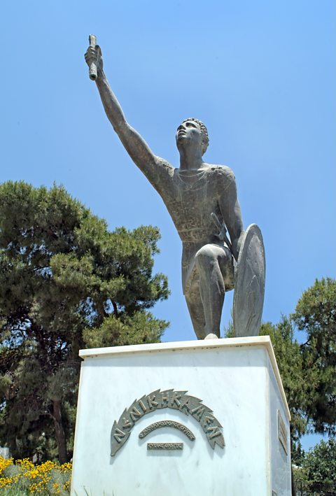 A statue of Pheidippides showing the soldier knelt on one leg with a scroll in his hand