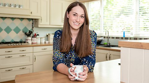 Kate Hall standing in her kitchen, leaning on a work surface with a cup in her hands 