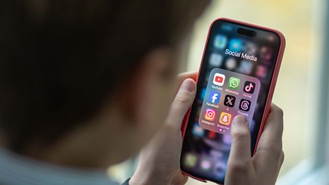 A young boy holding a smartphoe and looking at his social media apps.