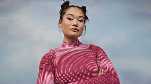 A self-confident and assured young woman wearing a pink sweater and pink eyeshadow staring down the lens.