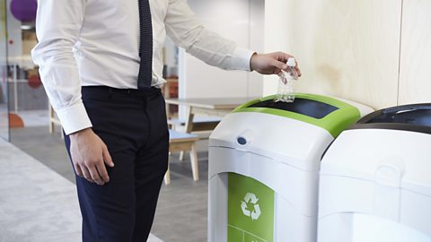 Man in an office throwing plastic bottle into recycling bin.