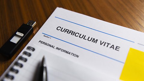 A printed copy of a CV with the personal information obscured by a notepad on top of it and a pen on top of the pad.