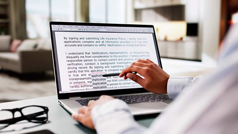 A woman sitting in her living room proof reading an application form on her computer screen - correcting spelling mistakes.
