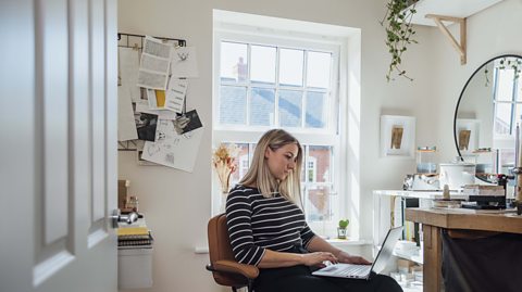 A female entrepreneur sitting in her workspace at home on her computer doing market research for her design business.