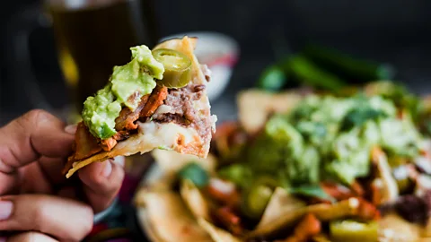 Getty Images Hand holding nacho chips with cheese and guac (Credit: Getty Images)