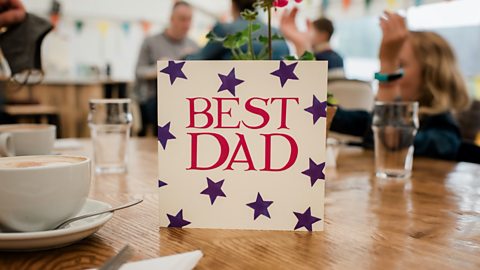 A card on a table that reads 'best dad' in pink writing with purple stars