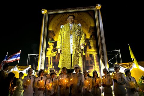 A huge portrait of a Thai king is set up on a stage which people holding calendars below 
