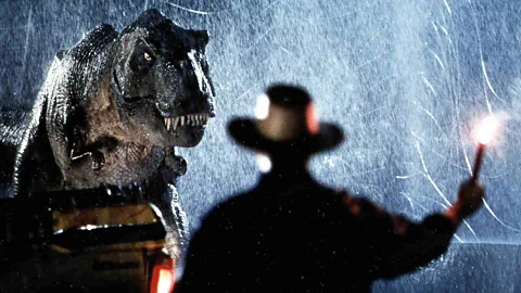 Alamy A man with a flare looking at a T-Rex in a scene from Jurassic Park (Credit: Alamy)