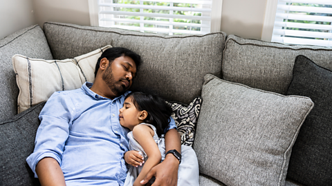 A father and daughter sleep on the sofa together.