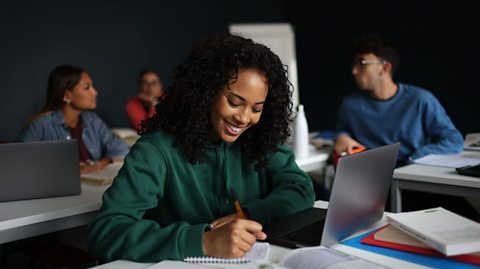 Girl of black heritage smiling and writing down notes on a table or desk at school