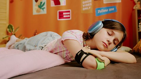 Teenager sleeping on bed with blue headphones on.