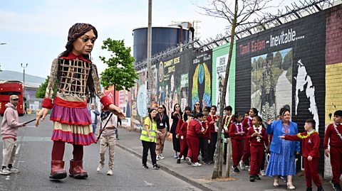 Little Amal the 12-foot-tall puppet symbolising children of war - walking along the Peace Walls in Belfast guided by local children.