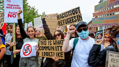 Protestors at an anti-racism march hold up signs saying 'migrants welcome' one saying 'this is what community looks like, 'racists out refugees in'.