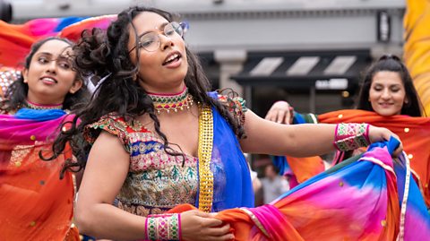 Annual Mela Carnival Parade - three young Indian women dressed in colourful traditional clothing dancing in city centre.