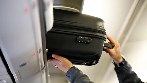 A carry-on suitcase being placed into an airplane's overhead compartment Credit: Alamy