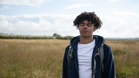 A young boy going for a walk in a field - closing his eyes and practising mindfulness.