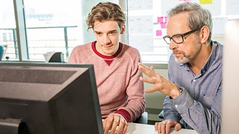 An apprentice being shown what to do on a computer screen by a colleague.