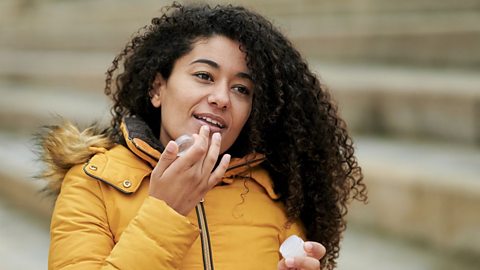 An image of a young female pinch agelong acheronian curly hairsbreadth applying articulator balm from a mini tin while outside