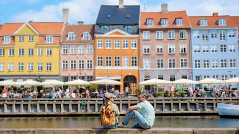 Getty Images Two people sit by the canal in Copenhagen in front of colourful buildings (Credit: Getty Images)