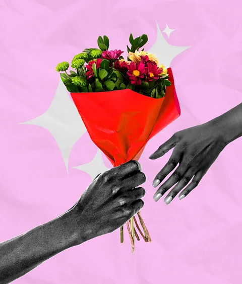 Serenity Strull/ Getty Images An arm holding out a bouquet of flowers to another hand, with diamond-shaped sparkles against a pink background (Credit: Serenity Strull/ Getty Images)
