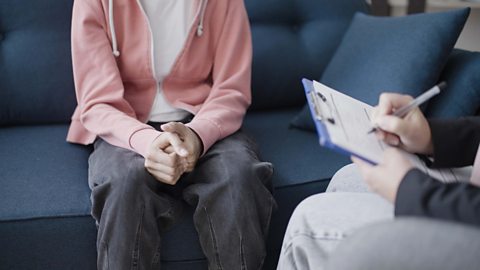 A young person sitting on a sofa talking to a councillor with a clipboard in their hands filling in a questionnaire.