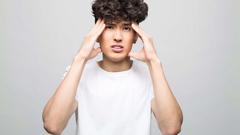 Young malewearing a white t-shirt - holding his hands up to his temples indicating a stress headache.