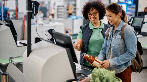 A supermarket member of staff helping a customer self-scan their shopping.
