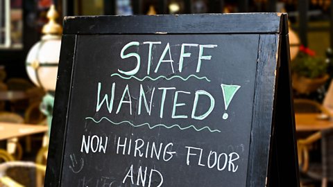 A chalkboard sign outside a bar saying 'Staff wanted. Now hiring floor and...'