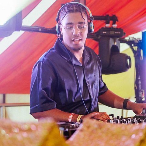 Aidan Hammond playing music as a DJ on stage with decoration and lights in shot.