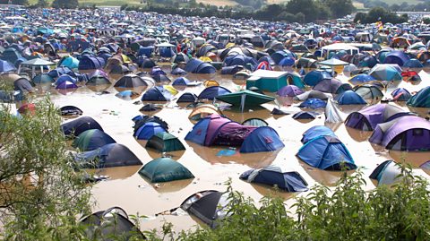 Festival campsite flooded after heavy rain, with tents partially submerged in muddy water in a rural outdoor setting