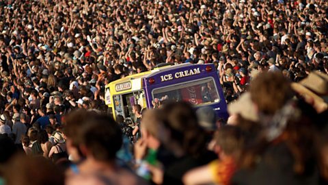 Large crowd at a summer music festival with an ice cream van serving cold drinks in the centre of the gathering