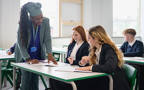 A teacher helps a group of GCSE students in a school classroom