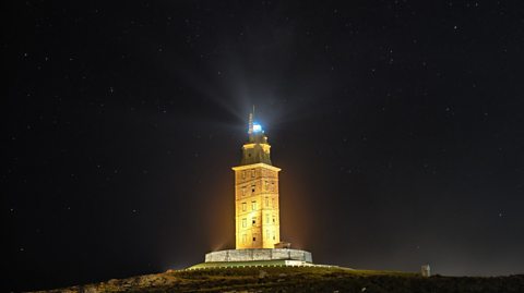 The Tower of Hercules shines bright against the night sky, the tower is lit and the lighthouse beacon illuminates the sky