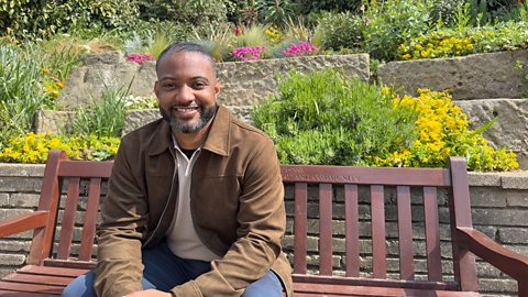 JB Gill sat on bench in a flower garden 
