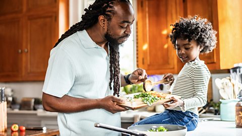 A father and son work together in the kitchen, frying some vegetables.