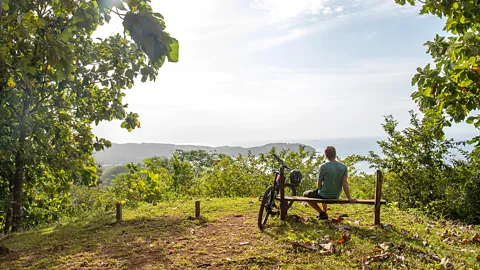 Getty Images Mountain biker relaxes on wooden bench in Panama with ocean in the distance (Credit: Getty Images)