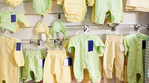 A retail wall stocked with pale yellow and mint green baby clothes 