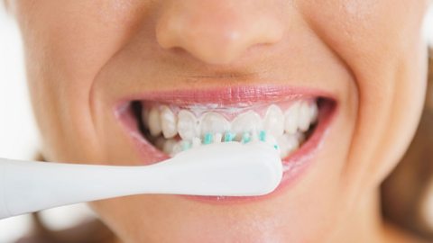 A woman brushing her teeth using brush and toothpaste
