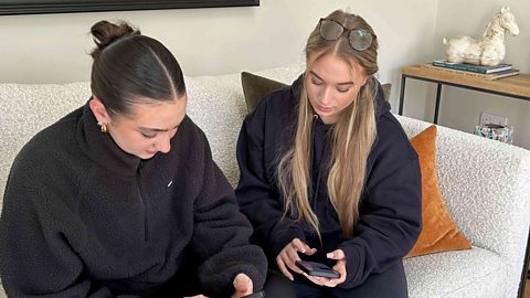 two young women on a sofa looking at their mobile devices.