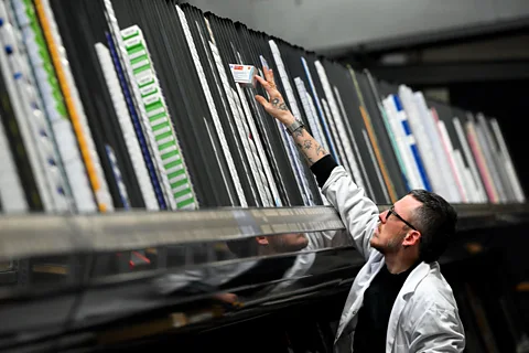 Getty Images An employee at a pharmaceutical warehouse in a white coat reaches for a box of medication (Credit: Getty Images)