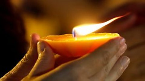 A close-up of two hands holding a tea-light candle