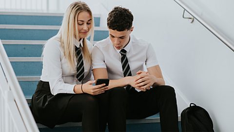Two students looking at a phone in the school corridor.