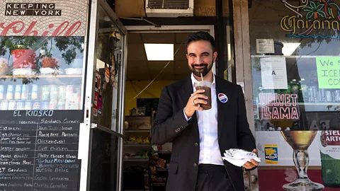 Getty Images Zohran Mamdani smiles standing outside of a NYC bodega, holding an iced coffee and a sandwich (Credit: Getty Images)