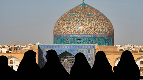 A group of women look out from a balcony over a mosque.
