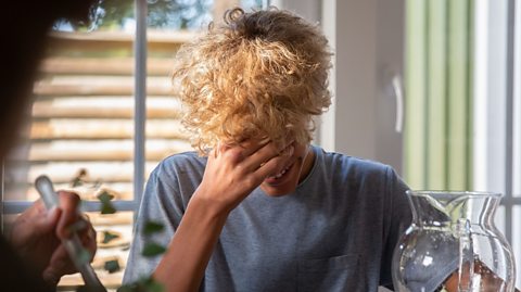 Boy laughing with his head down and hand over his face