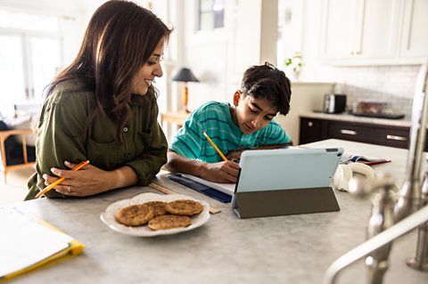 A mum sits with her home educated son at the kitchen table as he studies 
